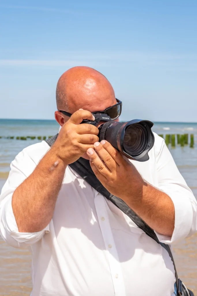 Fotograaf Dick van der Veer in actie met zijn fotocamera op het strand in Zeeland